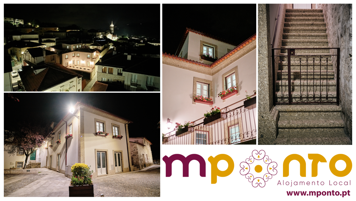 The image captures a well-lit view of a charming neighborhood at night, showcasing buildings adorned with flower boxes. A staircase with a wrought iron railing leads to a doorway, framed by stone walls, while a distant clock tower is visible against the night sky.