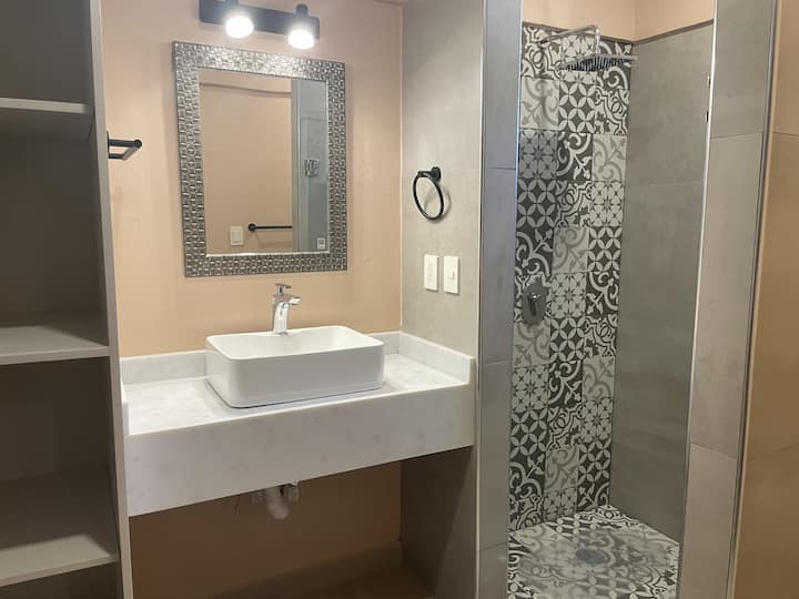 El baño a ras de suelo combina estilo y funcionalidad, con un moderno lavabo con estanterías abiertas, una elegante ducha de azulejos con puertas de vidrio y una zona de inodoro separada. El espacio es luminoso y bien organizado, y ofrece una experiencia cómoda y práctica
