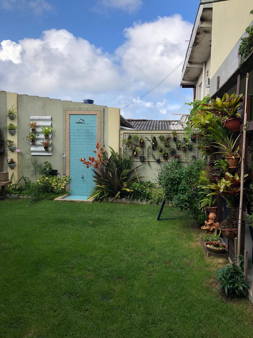 A serene garden area is depicted, featuring lush green grass and various potted plants along the walls. A vibrant blue door is centrally placed, surrounded by decorative flora, while a collection of vertical planters adds natural texture to the backdrop.