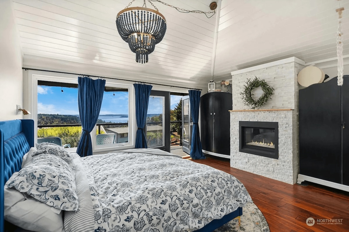 Master bedroom with vaulted ceilings, a smart TV, and water views. Features a king-size bed, bedside lights, and a private entrance to the patio/deck. Enjoy cozy nights by the indoor fireplace in this elegant space.