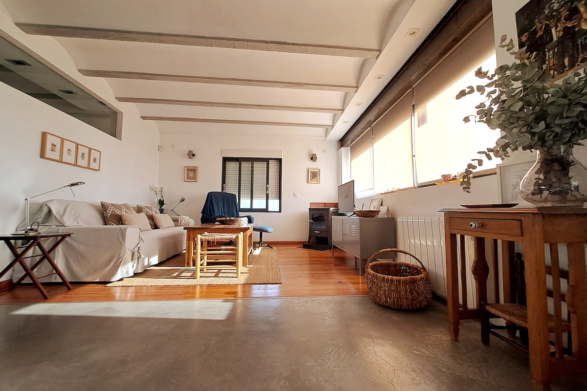 A well-lit living area features a comfortable sofa draped with a light cover. A wooden coffee table sits near a wicker basket, complemented by natural light streaming through large windows. A subtle blend of textures creates a serene environment, highlighted by minimal decor.