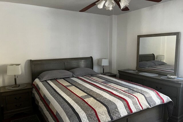 A spacious bedroom is furnished with a large bed adorned with a striped quilt. A dresser and two bedside tables are present, each topped with a lamp. A wall-mounted mirror reflects the room's light and enhances the sense of openness.