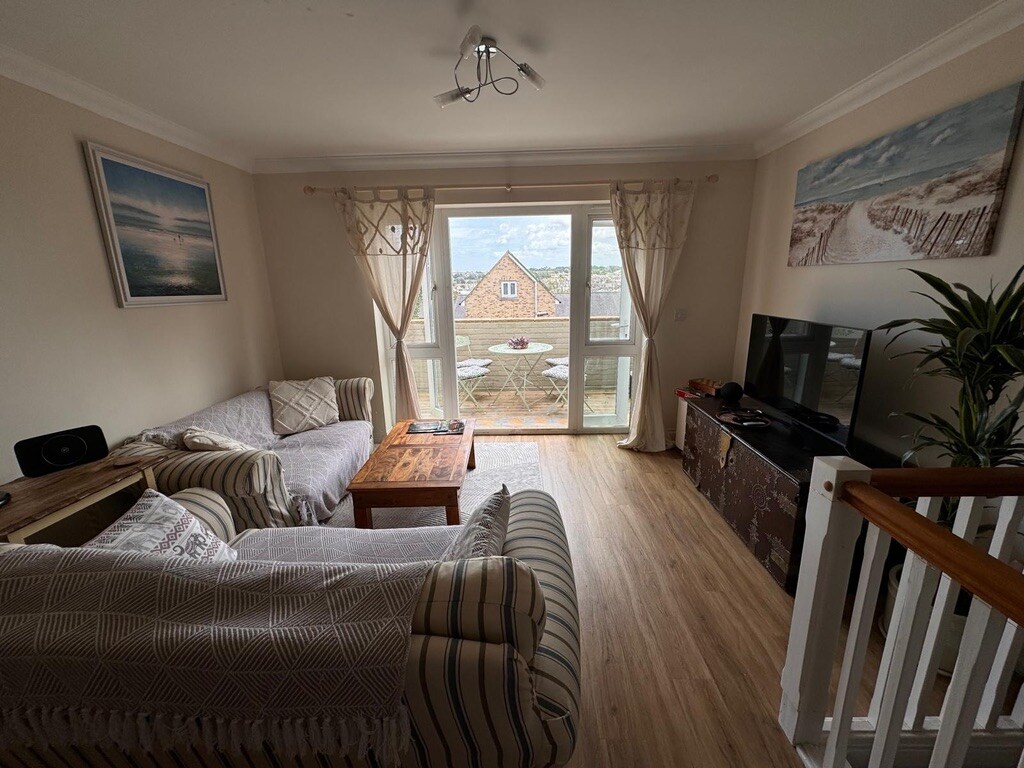 The living area showcases two comfortable sofas arranged around a wooden coffee table. Large, east-facing windows provide views of the outdoors, filling the space with natural light. A television is positioned on a cabinet, contributing to the inviting setting.