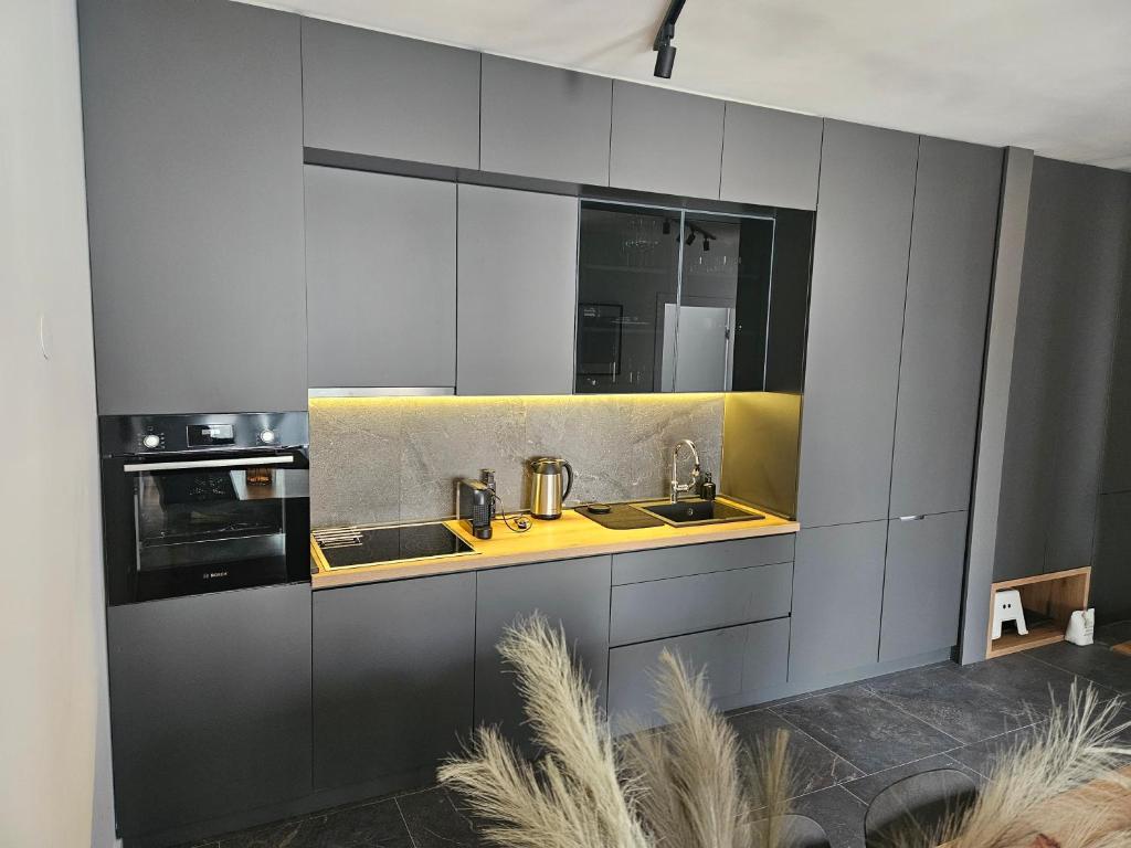A sleek kitchen area is presented with modern cabinetry in dark tones. The countertop is enhanced by warm under-cabinet lighting, illuminating the cooking appliances, including a built-in oven and stovetop. A minimalistic sink and various utensils are arranged neatly for convenience.