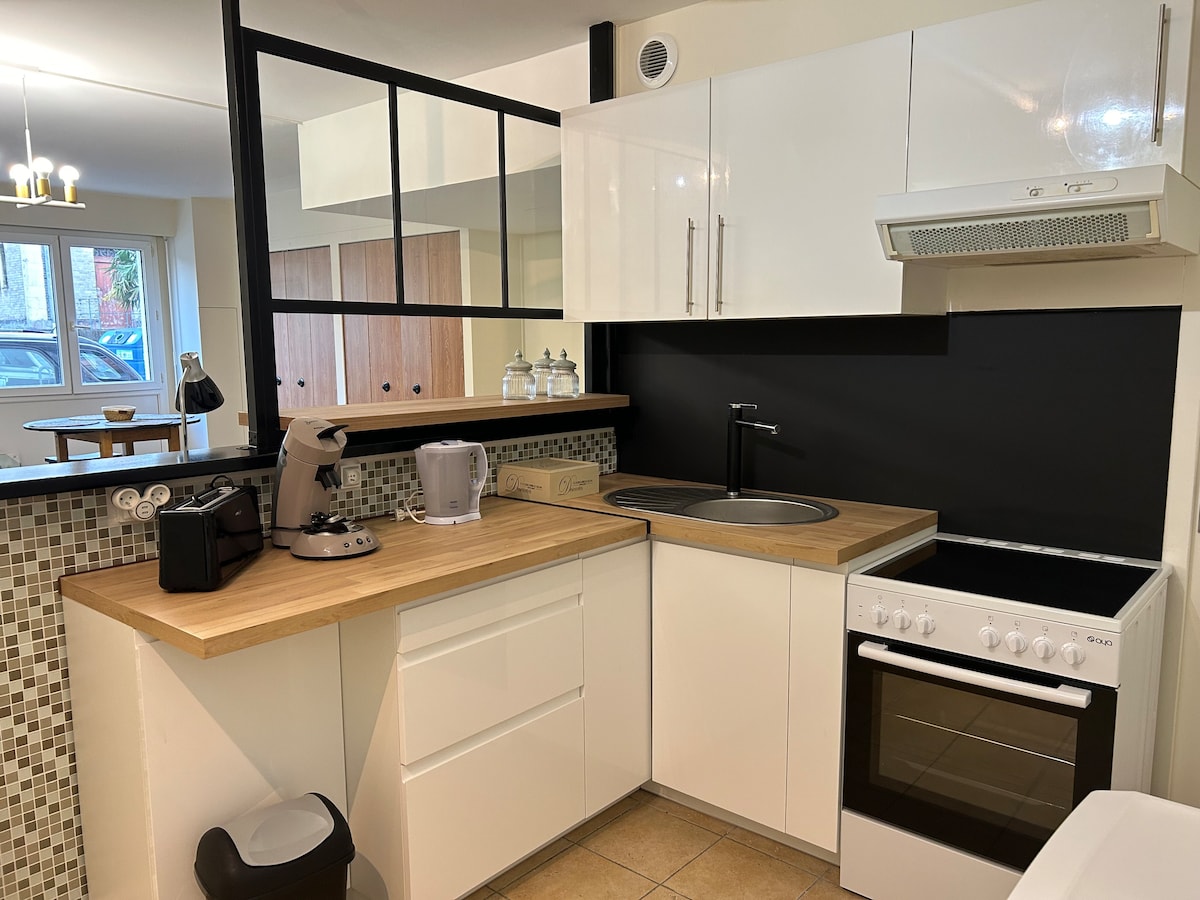 A functional kitchen is shown, featuring modern cabinetry and a light wood countertop. Essential appliances including a stove, microwave, and coffee maker are visible. A mosaic backsplash adds texture, while a large window allows natural light to brighten the space.