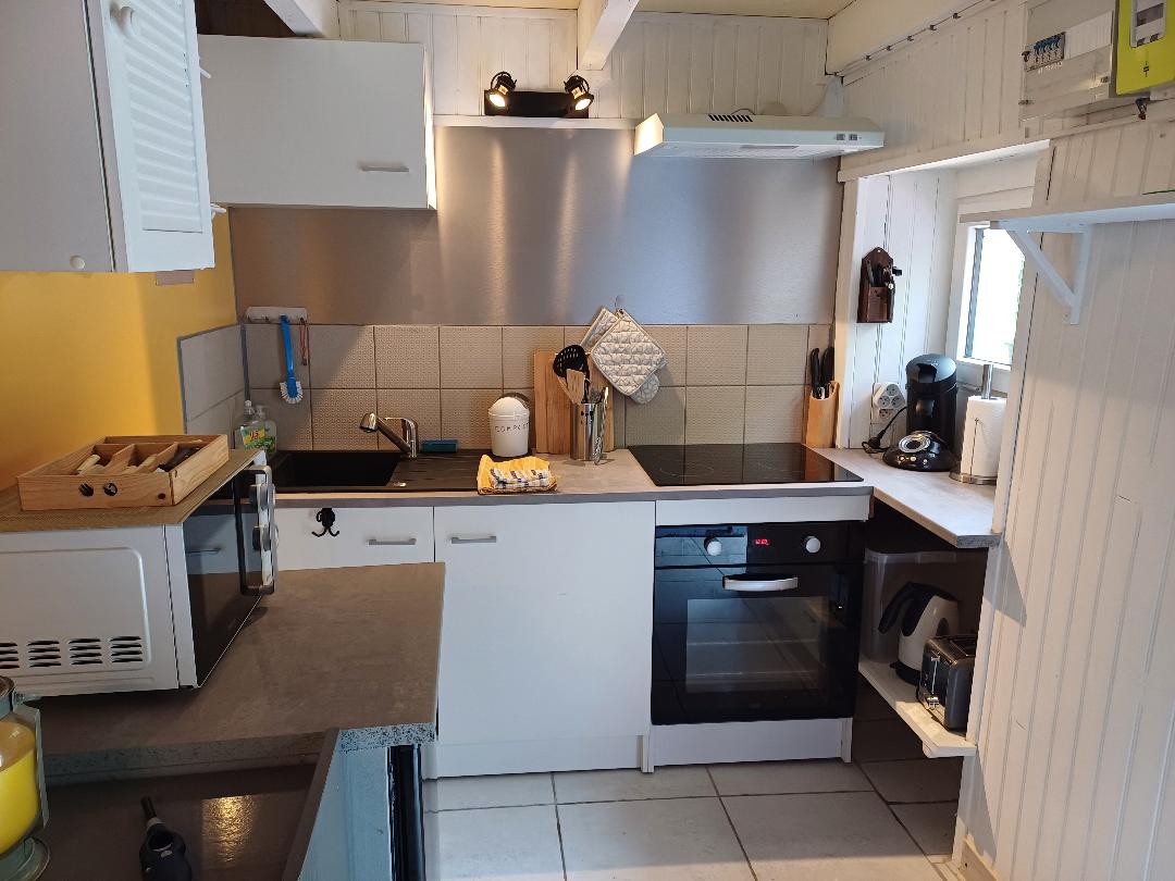 The kitchen is equipped with a modern cooktop, oven, and microwave. Sleek cabinets and a countertop create a functional cooking space. Utensils and small appliances are organized neatly, while natural light fills the area through a small window.