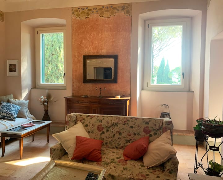 Obývacia izba. Pokiaľ ide o architektonický štýl, tento apartmán sme zrekonštruovali zachovaním starobylej omietky, typickej terakotovej podlahy a stropov vyzdobených v chladnom secesnom štýle z 19. storočia.