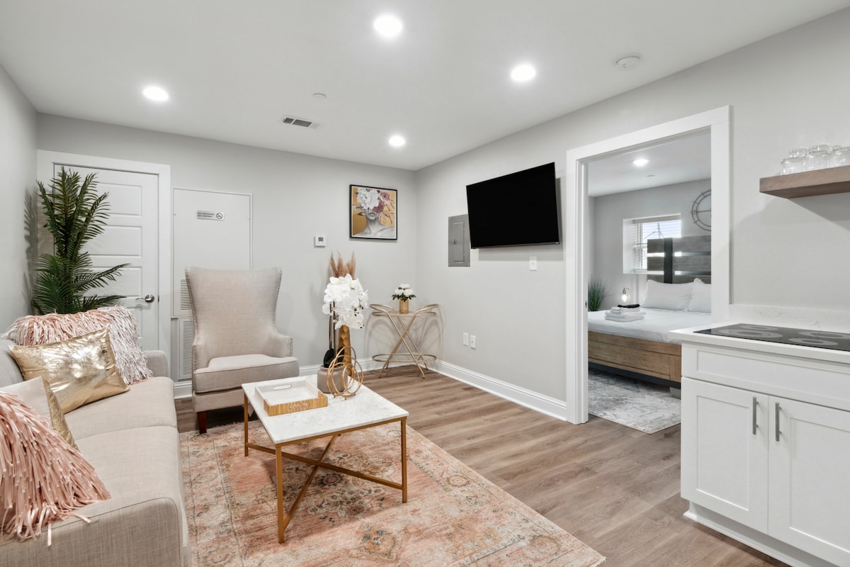 Unit 2C Woonruimte in slaapkamer, aan de muur gemonteerde smart HDTV met streamingdiensten, bank en stoel om te zitten, met zorg ontworpen, naast de keuken