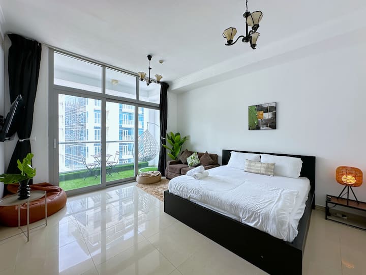 Sehemu ya kuishi iliyo na kitanda na mapambo madogo, pamoja na poufs na vitu vingine, vyote vikielekea kwenye roshani, na kuunda mazingira angavu na ya wazi