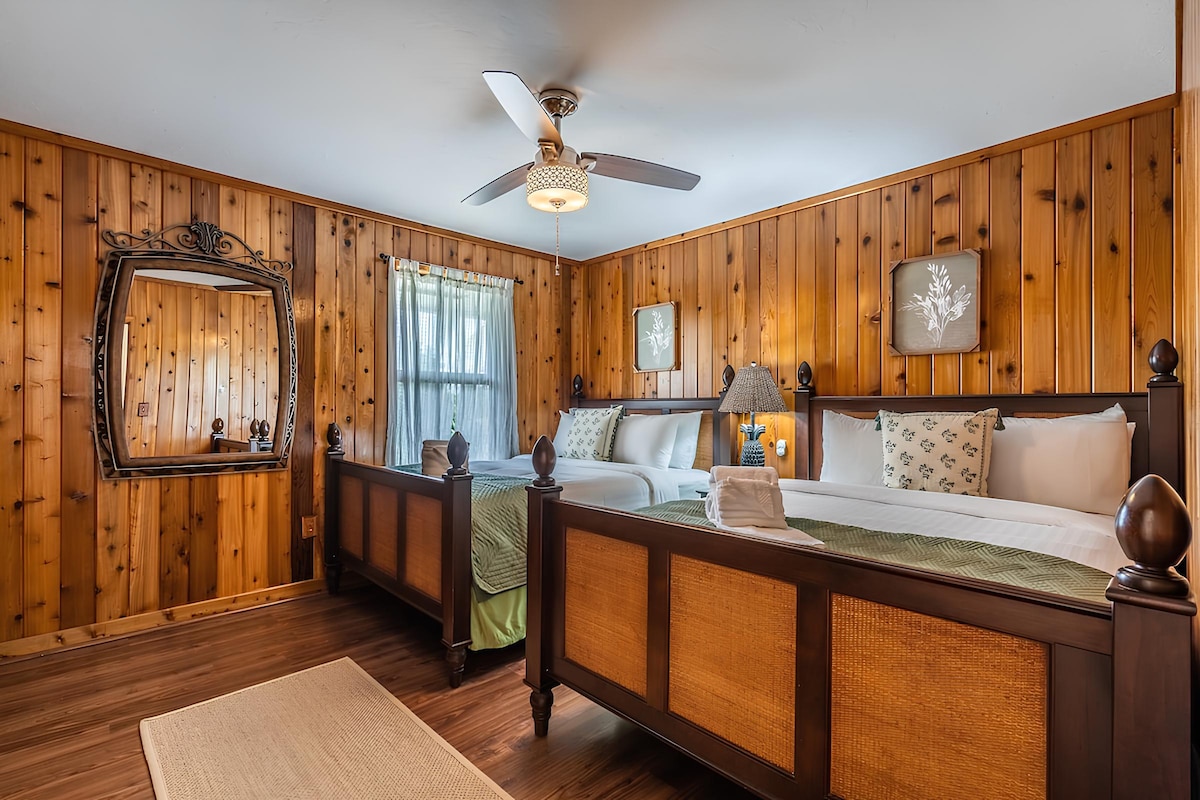 Cozy twin bedroom with wood-paneled walls, featuring comfortable beds, soft lighting, and a large mirror. The room also includes a spacious closet and a built-in bookshelf for added storage and relaxation.