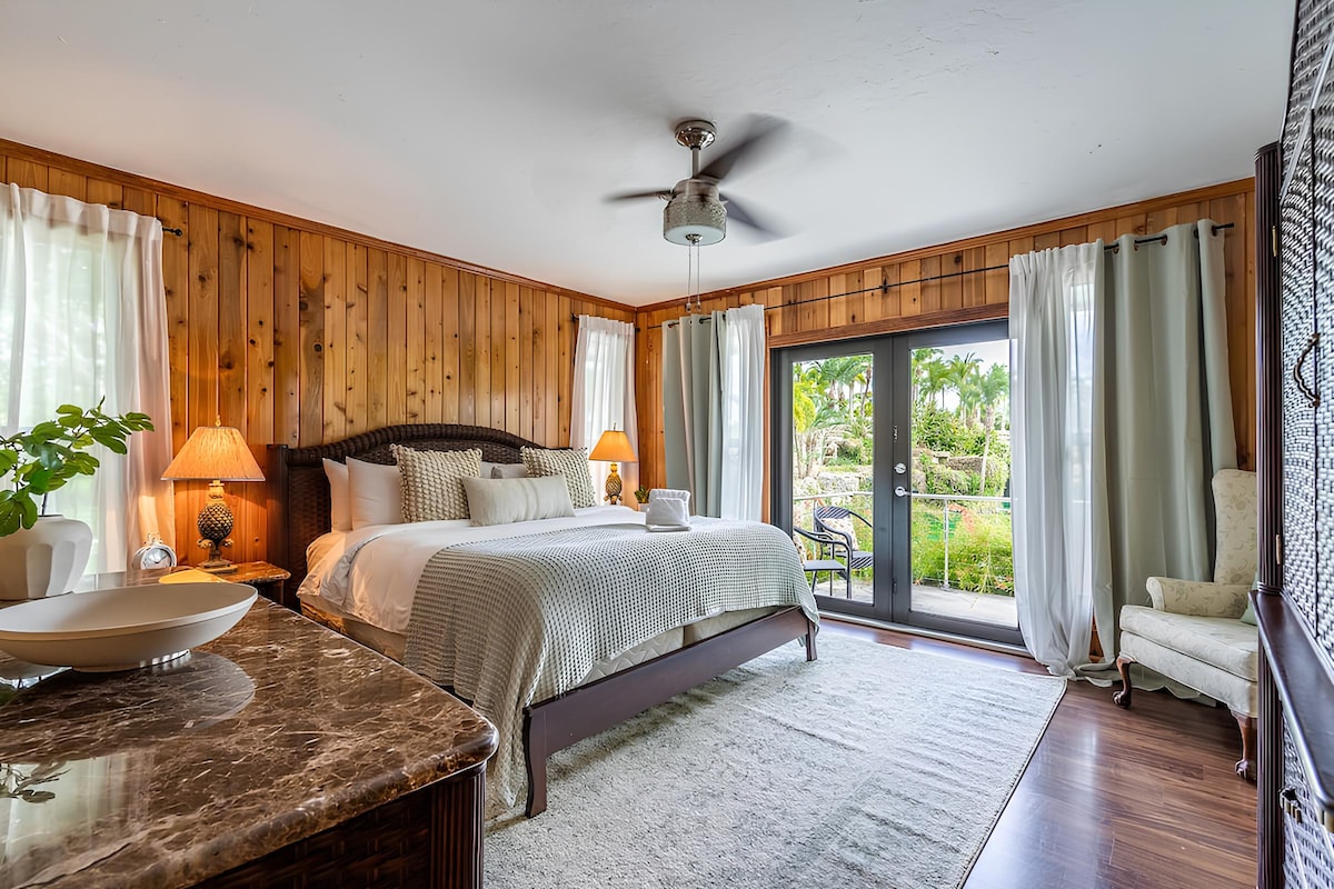 Cozy bedroom with wood-paneled walls and a comfortable king-size bed. Large glass doors open to the outdoors, offering a peaceful view, perfect for enjoying morning coffee.