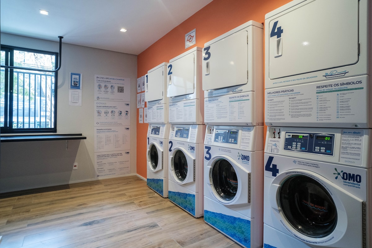 A laundry room is presented with multiple washing machines, each numbered for easy identification. Clear instructions are displayed on the wall, alongside information regarding laundry symbols. The space features soft lighting and a neutral color palette, providing a clean and organized appearance.