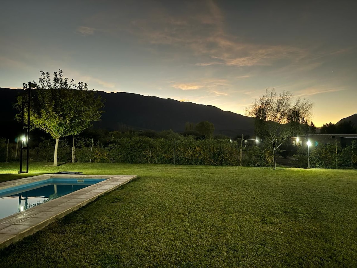 A serene outdoor area is highlighted by a private pool, framed by a neatly maintained lawn. Surrounding trees and soft lighting create a calm ambiance, with mountains visible in the distance under a twilight sky.