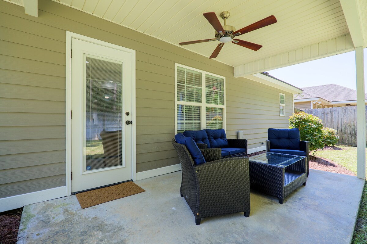 The back porch features a comfortable seating arrangement with two armchairs and a coffee table. A ceiling fan is positioned above, providing a cooling breeze, while sunlight filters in through the glass door, enhancing the inviting outdoor space.