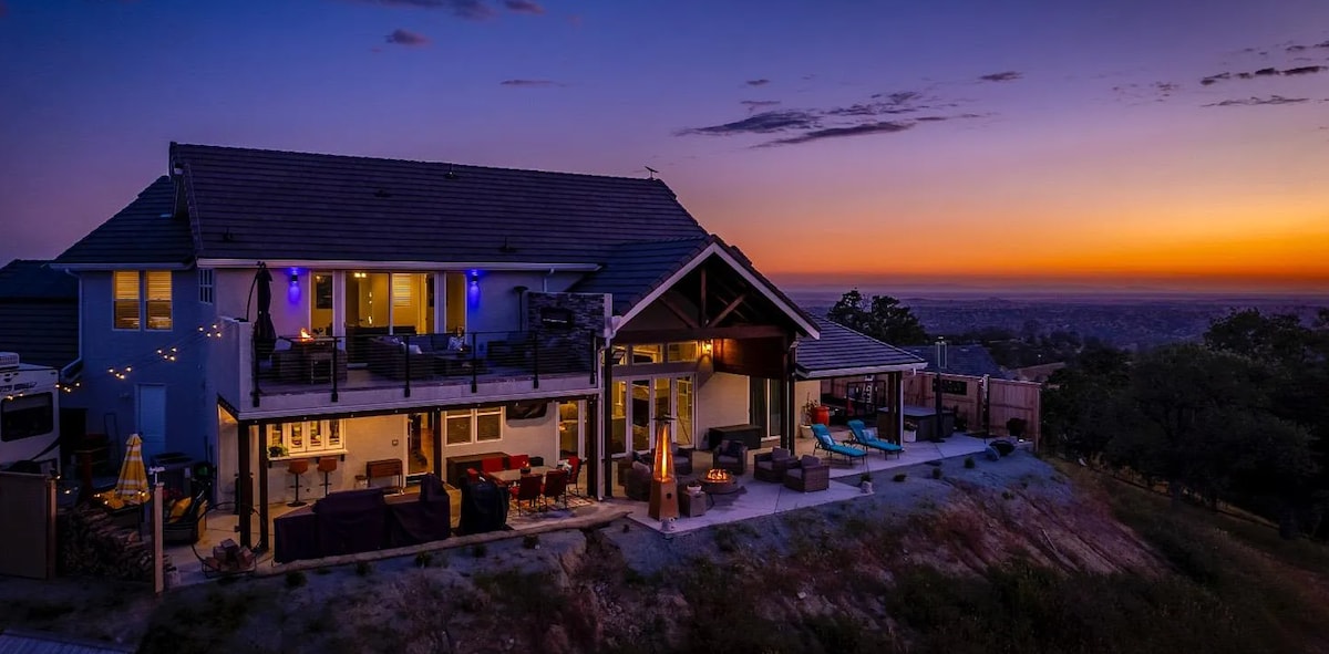 The exterior of the home is illuminated by soft lighting as twilight descends, showcasing a modern design with expansive outdoor patios. A stunning sunset paints the sky in hues of orange and purple, offering a serene backdrop for evenings spent in the outdoor seating areas.