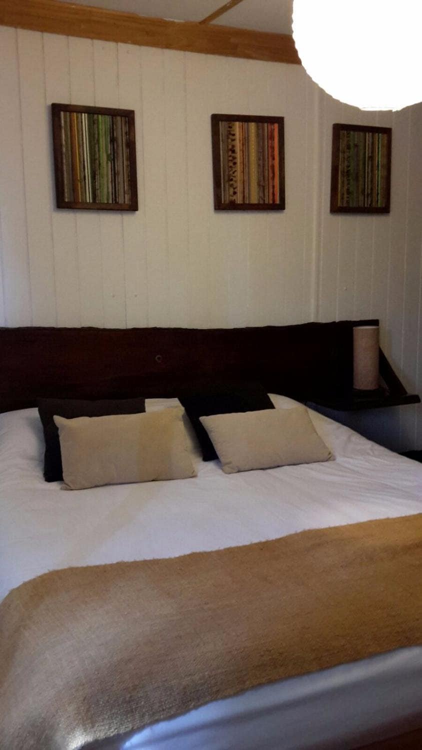 A cozy sleeping area is presented with a spacious bed adorned with neutral-colored pillows. Warm-toned artwork is displayed on the walls above the headboard, adding a touch of character. Soft lighting is provided by a pendant fixture overhead.