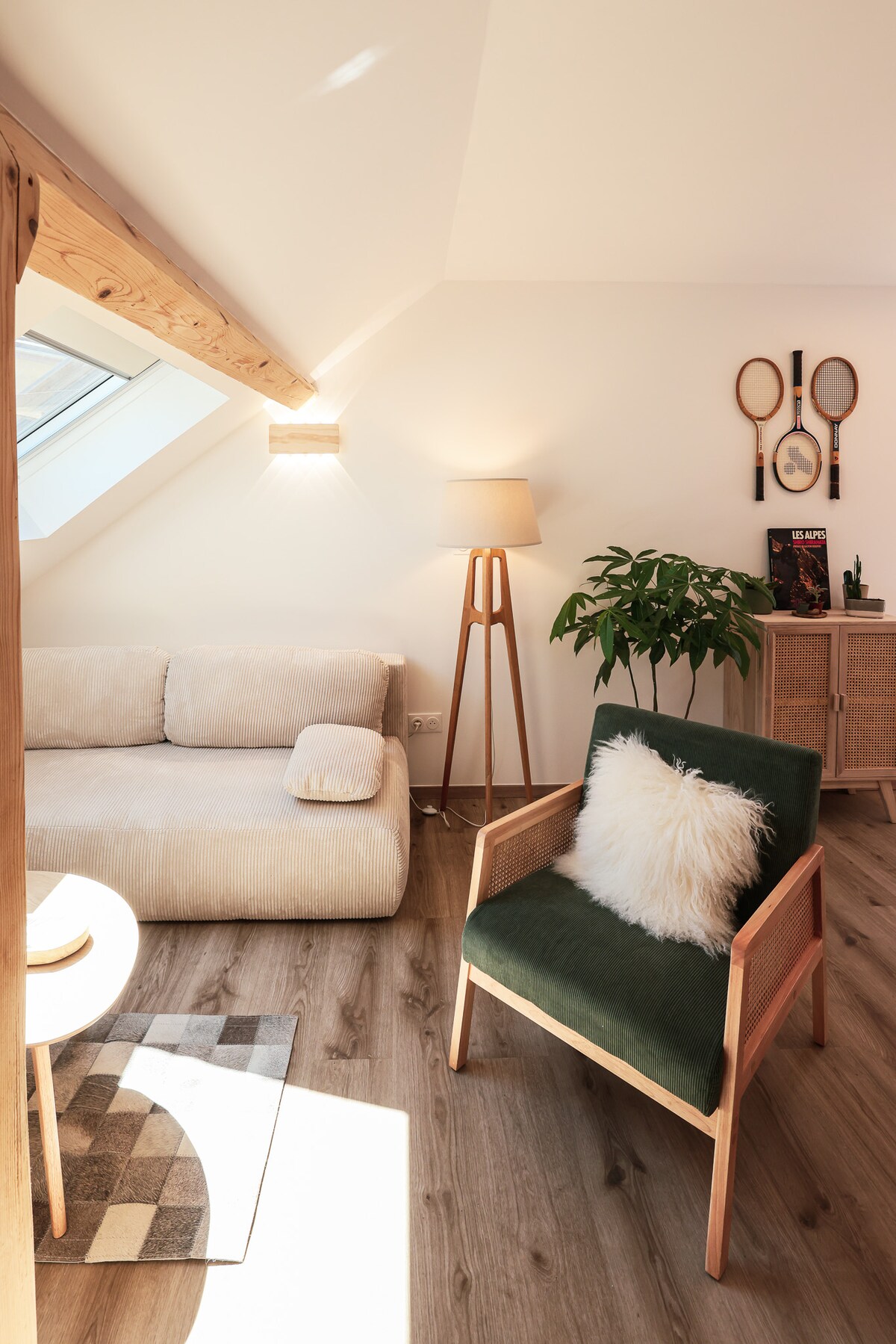 A well-lit living area is highlighted by a soft, beige sofa and a green-accented armchair. A floor lamp casts a gentle glow, while decorative elements, including plants and wall art, add character. Natural light enters through a skylight, enhancing the inviting space.