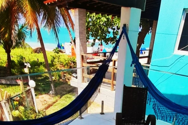 A patio area is depicted with a hammock hanging between two posts, accompanied by a wicker chair. Lush greenery and a glimpse of the beach can be seen in the background, creating a serene outdoor space.