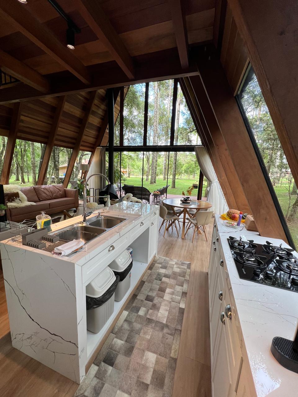 A spacious kitchen is framed by large windows, allowing natural light to illuminate the area. The kitchen features a modern countertop with a sink and stovetop, complemented by stylish cabinetry. A cozy seating area with a sofa is visible, along with a dining table adorned with a fruit centerpiece.