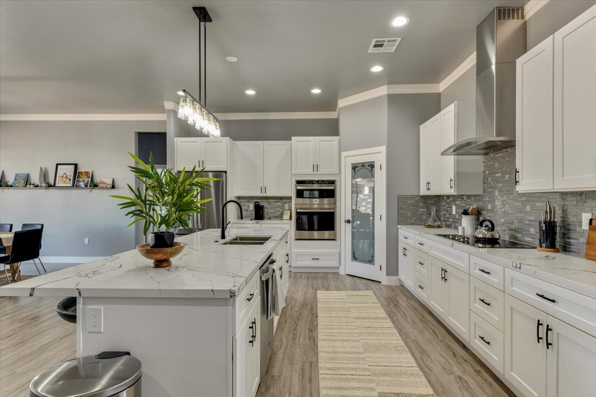 A spacious kitchen features modern white cabinetry and a large island topped with white marble. A subtle backsplash in soft grey complements the decor. Stainless steel appliances, including a fridge and oven, are integrated into the design, creating a functional and inviting cooking space.