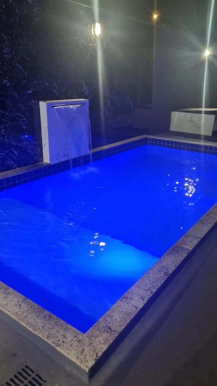 A tranquil pool is featured, illuminated in shades of blue. A sleek water feature adds a gentle flow, enhancing the serene atmosphere. The surrounding area is designed for relaxation and enjoyment, with a modern edge reflected in the pool's clean lines and contemporary materials.