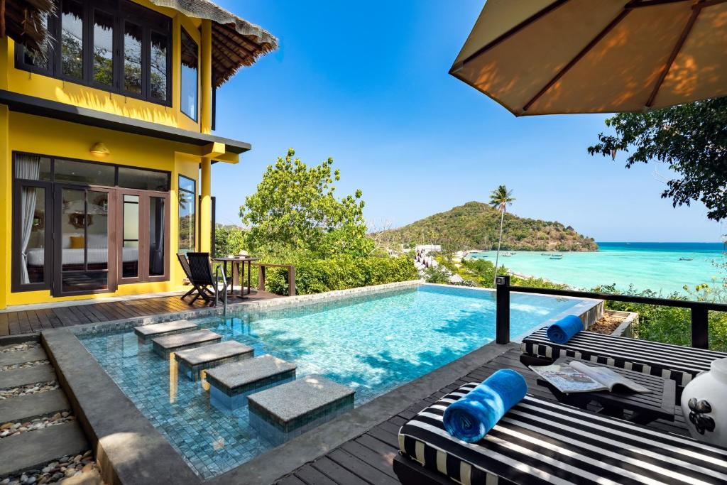 A private terrace showcases a stunning plunge pool surrounded by lush greenery, with stepped access leading to the water. Lounge chairs, equipped with thick blue towels, sit nearby under a large umbrella, offering a view of the turquoise waters and distant lush hills.