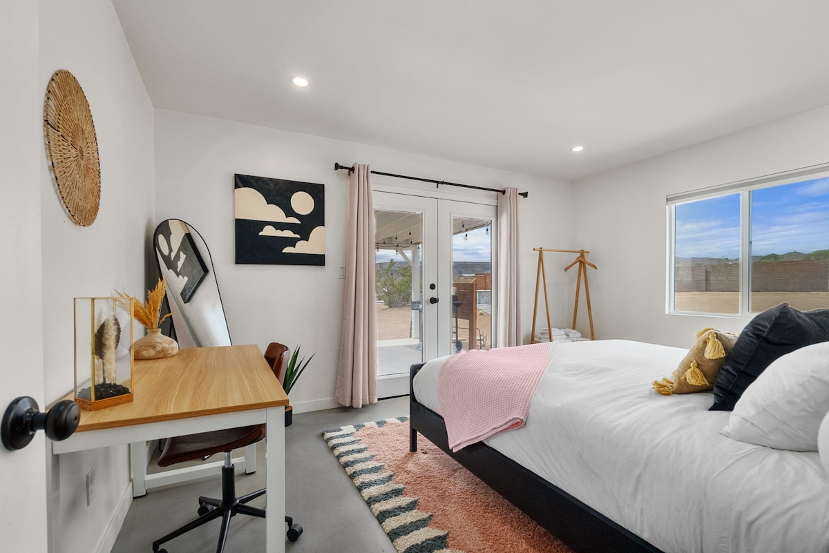 Светла и модерна спалня с голямо двойно легло, вдъхновена от пустинята, с луксозно спално бельо и достъп до вътрешен двор за сутрешно кафе или вечерно наблюдение на звездите.