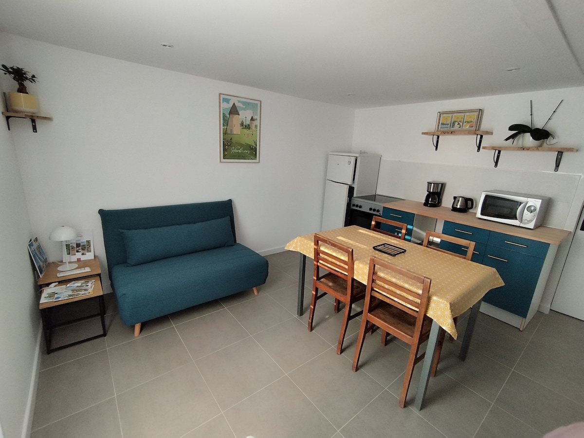 A spacious living area combines a comfortable sofa and dining table with wooden chairs. The kitchen features modern appliances, including a refrigerator, coffee maker, and microwave. Light-colored walls and tiled flooring contribute to the bright, functional ambiance.