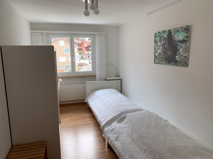 Schlafzimmer 2 mit zwei Einzelbetten, Schrank, Schreibtisch, Stuhl und Ablage für Gepäck.