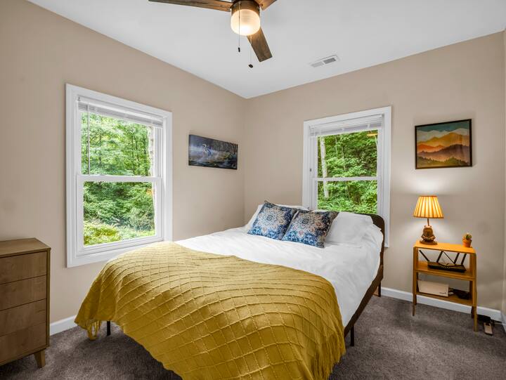 This serene bedroom features a queen-size bed and a private 1/2 bath, designed with the natural beauty of Lake Lure in mind. Earthy tones and rustic accents create a peaceful ambiance, offering a cozy, relaxing retreat after a day of exploring.