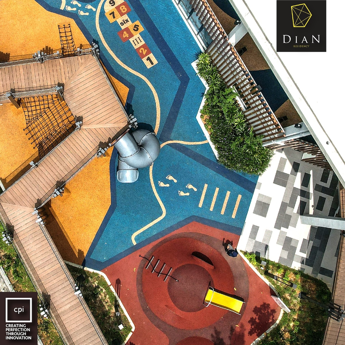 Aerial view of a vibrant outdoor playground featuring colorful surfaces, pathways, and various play structures. Different areas are designated for activities, with slides, climbing frames, and open spaces surrounded by greenery and seating arrangements, providing an engaging environment for families and children.