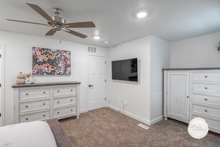 Pumzika katika chumba hiki cha kulala chenye utulivu kilicho na kitanda kizuri, fanicha nyeupe za kijijini, feni ya dari na televisheni ya skrini bapa iliyowekwa ukutani. Sauti zisizoegemea upande wowote huunda mazingira ya utulivu yanayofaa kwa ajili ya kupumzika.