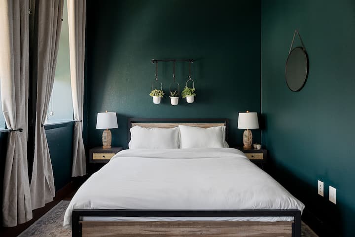 Este dormitorio sirve un ambiente tranquilo de retiro con sus paredes verdes profundas, su acogedora cama tamaño queen y el toque justo de vegetación . Es el lugar ideal para relajarse, recargar energías y tal vez dormir demasiado tiempo, porque ¿por qué no?