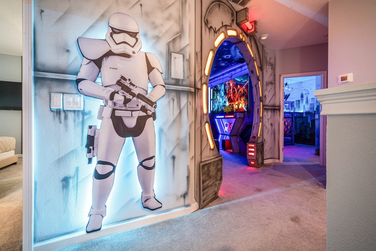 The entrance to the themed cinema room is highlighted by a vibrant mural of a Stormtrooper. An archway adorned with colorful lights leads into the entertainment area, where colorful artwork and decor contribute to a lively atmosphere.