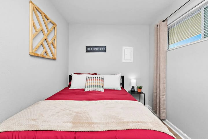 בחדר השינה הנעים הזה יש מיטה נוחה עם שמיכת פוך אדומה ושמיכה רכה. יש קיר עץ תלוי, חלון קטן עם וילונות ומנורה חמודה על שידת לילה.



