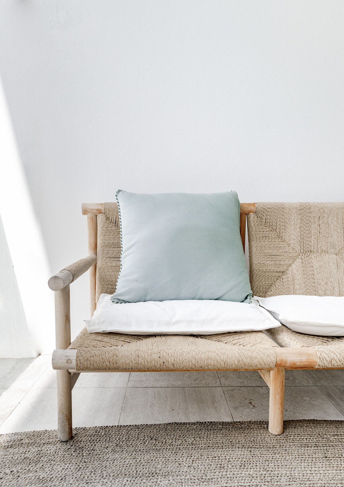 A woven lounge chair features a soft, light green cushion paired with a white accent pillow. Natural light enhances the calm aesthetic of the seating area, which is complemented by a textured rug beneath.