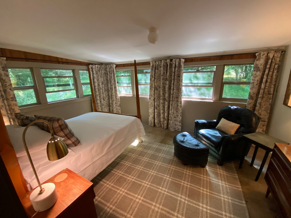 توفر النوافذ في غرفة النوم الرئيسية إطلالة مثالية على الغابة والجانب الجبلي. يوفر الكرسي المريح مكانًا رائعًا لقراءة كتاب والاسترخاء. 