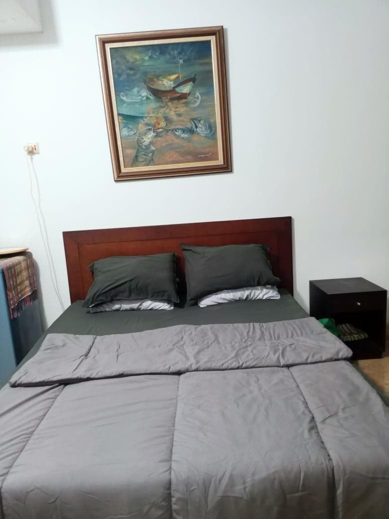 A cozy sleeping area is presented, featuring a spacious bed covered with a gray comforter. Two pillows sit against the headboard. A decorative painting hangs above the bed, and a nightstand is positioned beside it.
