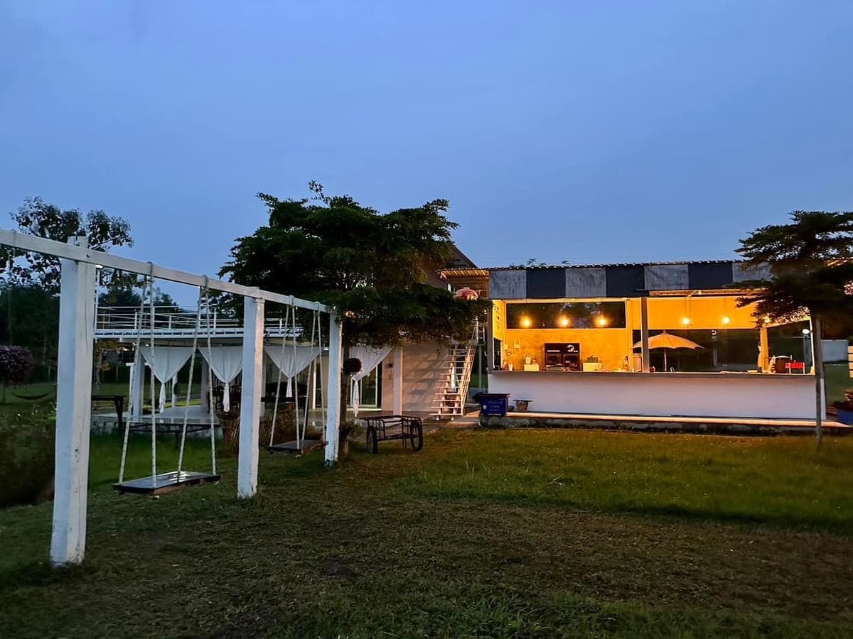 A modern, two-story structure is illuminated under twilight, showcasing large windows that offer views of the outdoor area. A swing set is positioned in the neatly kept lawn, with vibrant greenery enhancing the serene ambiance.