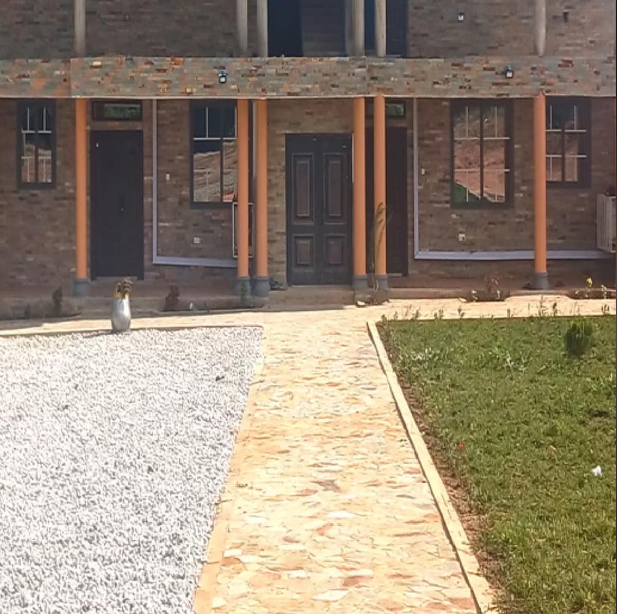 The exterior entrance features a neatly paved pathway leading to a dual-door entryway flanked by columns. The building is constructed with brick, and a landscaped area comprises both gravel and grass. The overall setting showcases a well-maintained property in a peaceful neighborhood.