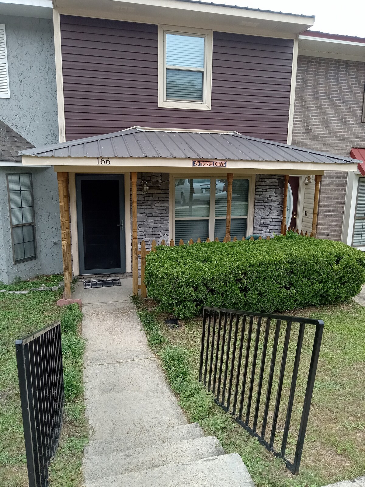 The entrance features a covered porch with a stone accent wall and a welcoming front door. A neatly trimmed bush enhances the landscaping, while a set of steps leads from the pathway to the porch. Railings flank both sides of the stairs.