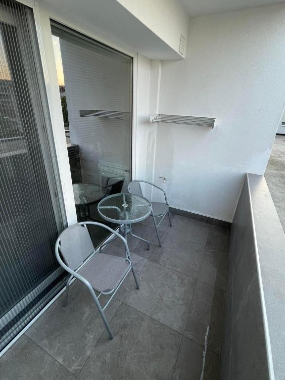 A cozy balcony features two metal chairs and a glass table, inviting relaxation while offering views of the surroundings. The clean tile floor and smooth walls create a minimalist aesthetic, with large sliding doors providing access to the interior space.