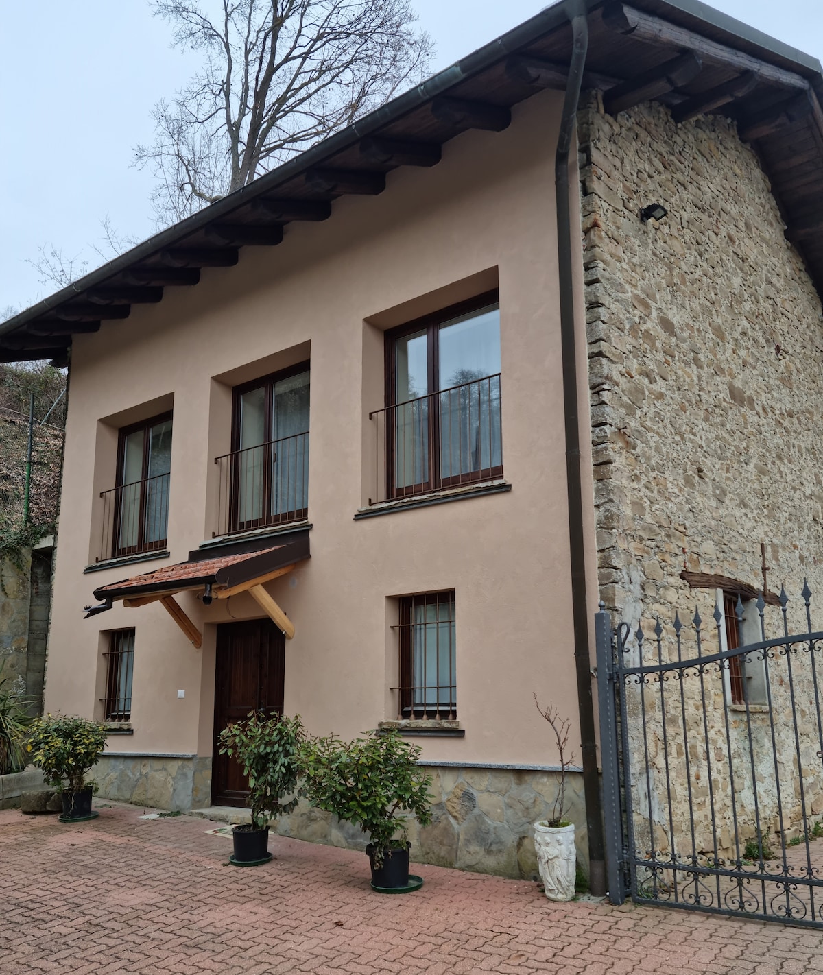 The exterior of the house displays a unique combination of smooth pink plaster and rustic stone. Large windows provide natural light, and wooden balconies add an inviting touch. Potted plants are positioned by the entrance, enhancing the home's connection to the surrounding natural environment.