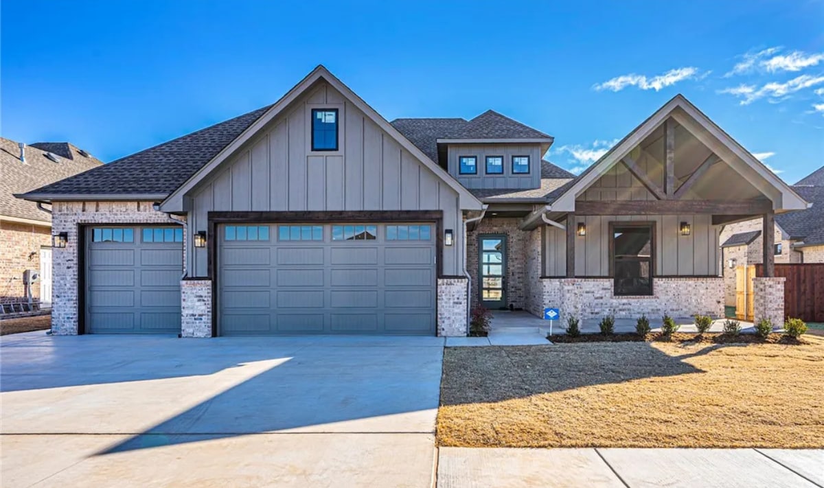 The exterior of the home features a modern design with a combination of stone and wood accents. A three-car garage is visible, with ample driveway space. The entryway is framed by large windows and a covered porch, complementing the overall architectural style.