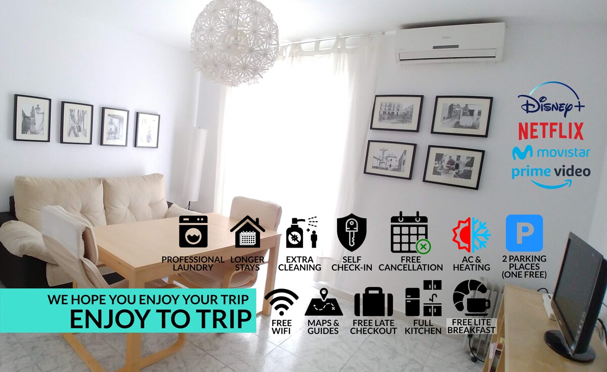 A well-lit living area features a large dining table surrounded by chairs, complemented by a comfortable sofa. Wall-mounted artwork adds character to the space. Air conditioning and heating units are visible, with a modern light fixture enhancing the ambiance. Icons indicate available amenities.