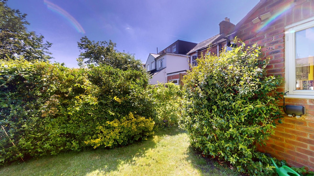 The spacious enclosed garden is surrounded by lush greenery, including various shrubs and small trees. A well-maintained lawn extends, offering a tranquil outdoor area. Natural sunlight illuminates the space, contributing to a serene environment suitable for relaxation or play.