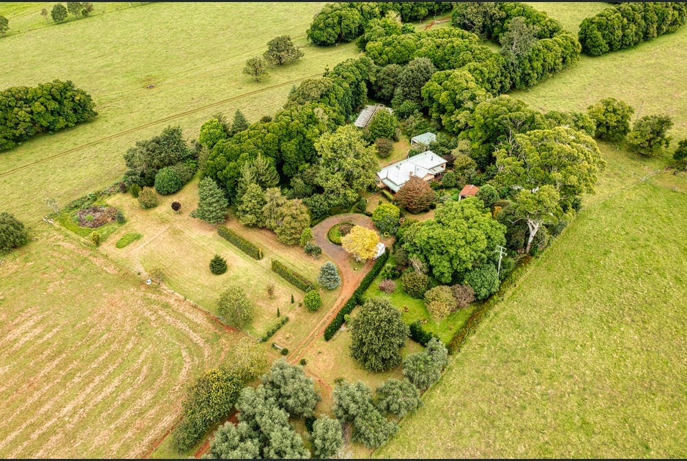 An aerial view captures the expansive property, revealing lush greenery and the layout of manicured gardens surrounding the main house. The landscape includes a mix of trees and open spaces, showcasing the natural beauty of the surroundings.