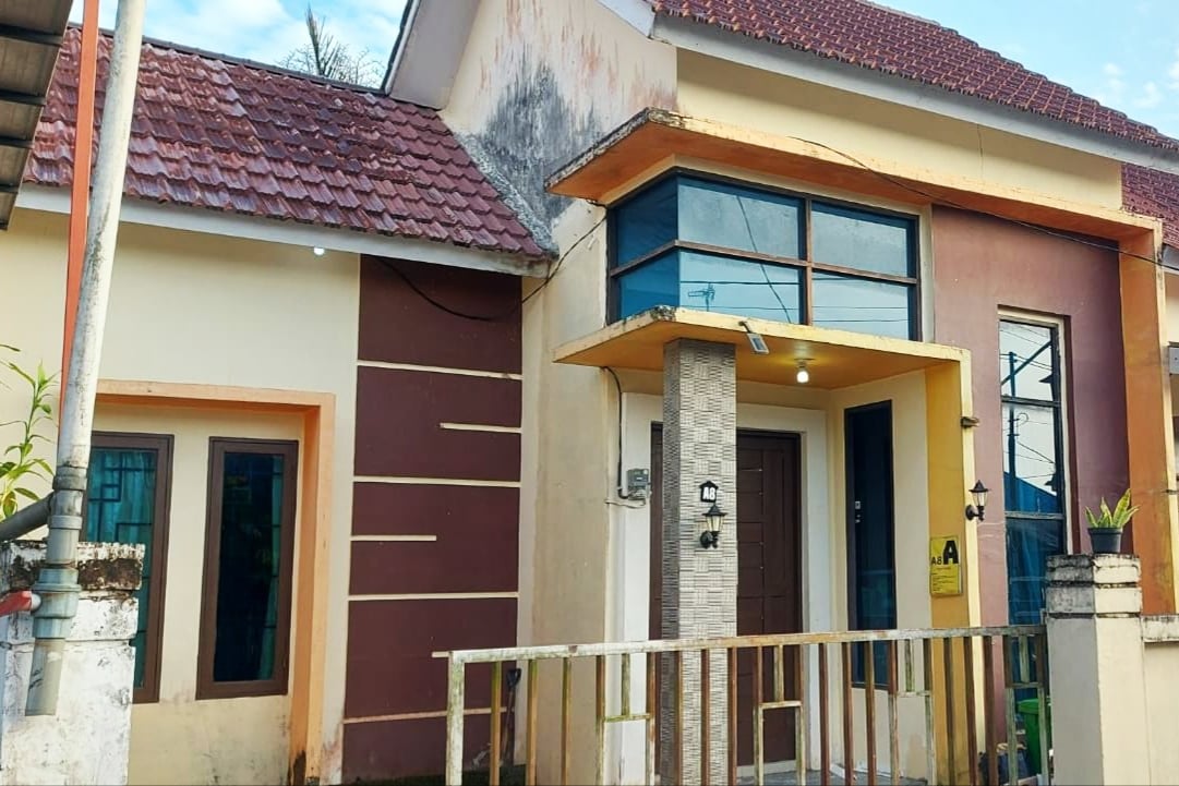 The exterior of the guest house features a modern design with a two-tone color palette. A covered entrance is highlighted by clean lines and large windows, allowing natural light to illuminate the entryway. Surrounding greenery offers a touch of nature to the setting.