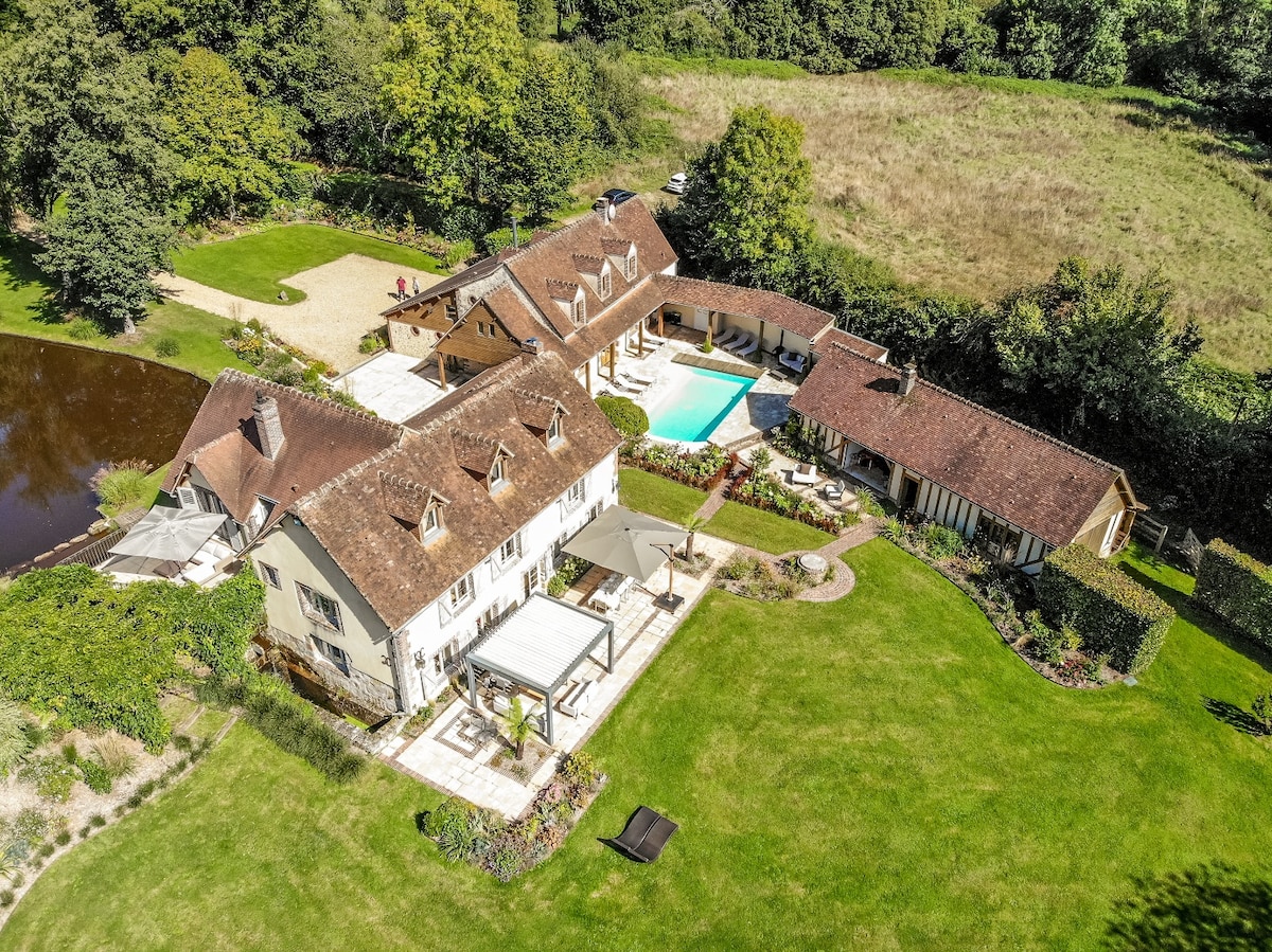An aerial view of the property showcases the spacious grounds, featuring a well-maintained lawn and a private pool. The two houses are highlighted, along with outdoor seating areas and the nearby serene pond, surrounded by a blend of trees and open space.