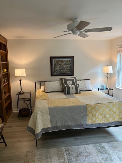 A comfortable sleeping area features a spacious bed covered with a light quilt in yellow and gray. Two bedside lamps provide warm lighting. A window dressed with blinds allows natural light, while a small bookshelf adds a touch of functionality to the room.